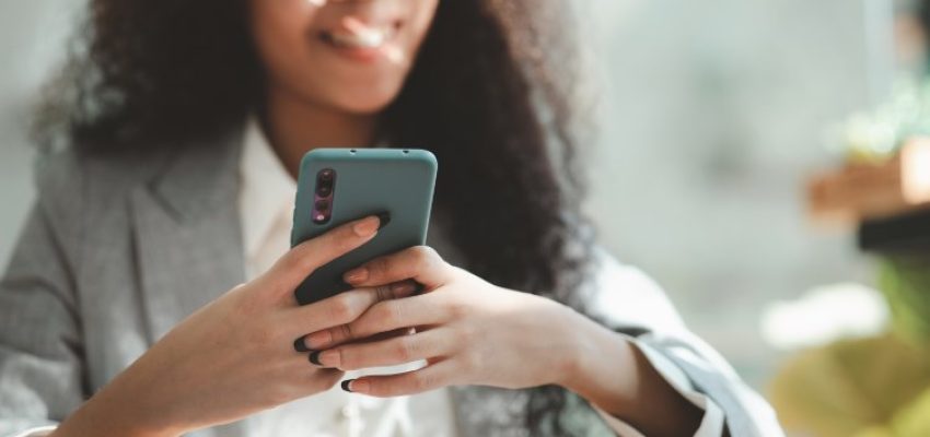 Close up american woman holding smartphone, she is using smartphone browsing social media and chatting with friends on online messaging app. The concept of using a smartphone.