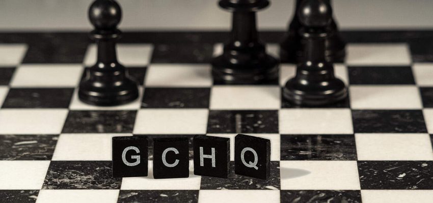 The acronym GCHQ for Government Communications Headquarters represented by black and white letter tiles on a marble chessboard with chess pieces